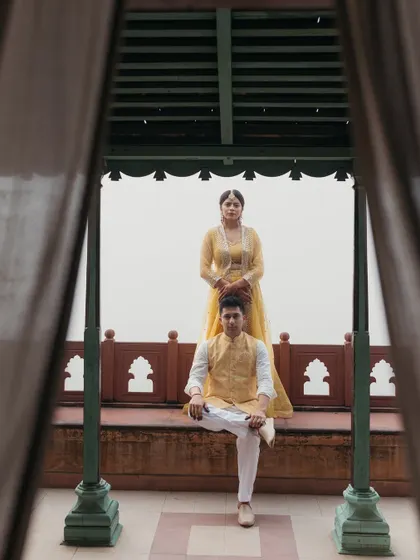 A creatively framed portrait of the couple during their Haldi ceremony at Neemrana, using curtains to create a sense of intimacy.