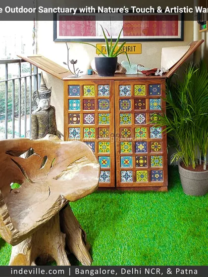 A vibrant and eclectic balcony nook. The space features a handcrafted wooden chair, a colorful tiled cabinet, and a serene Buddha statue, blending rustic, artistic, and spiritual elements into a cozy outdoor corner.