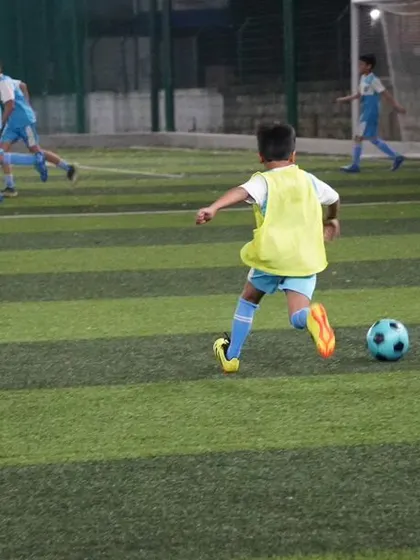 Young players in yellow bibs chase the ball during a small-sided game, learning positioning and teamwork.