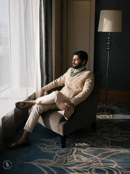 A classic groom's portrait. Seated by the window, the natural light creates a soft yet strong look, highlighting his elegant traditional attire and calm demeanor.