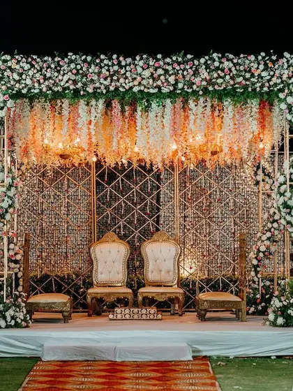 A surreal mandap design featuring a canopy of suspended florals and a geometric golden backdrop. The seating is regal, fit for a king and queen.