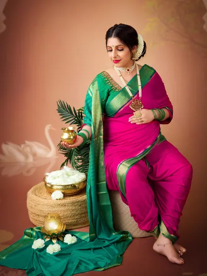 A solo portrait of the mother-to-be in a vibrant pink and green 'nauvari' saree. The traditional jewelry and props complete this beautiful cultural look.