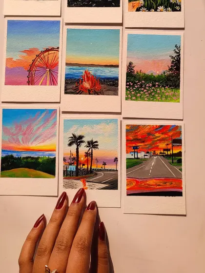 My hand reaching over a set of six vibrant landscape polaroids. Each one is a tiny, colorful world.