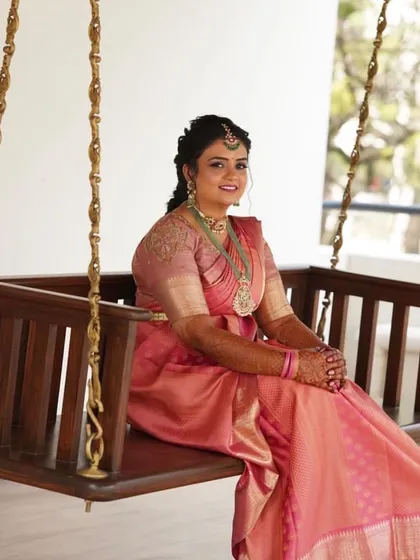 A candid moment of a bride on her special day. The saree is draped neatly, and her hair is styled in a traditional braid, showing a look that is both beautiful and comfortable.