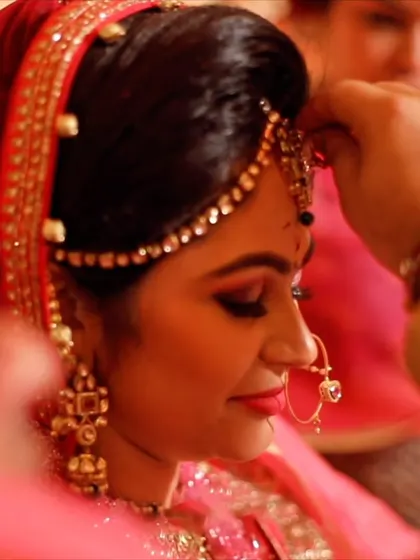 An intimate moment during the getting-ready process, as a maang tikka is placed on the bride's forehead.