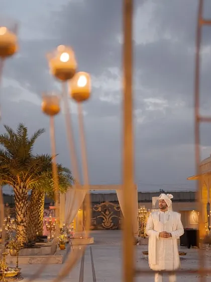 The groom stands alone amidst candlelit decor, waiting for his bride. This atmospheric shot captures the anticipation and the romantic, dreamy setup of the evening ceremony.