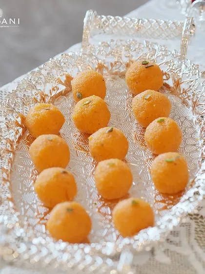 A silver tray laden with motichoor ladoo, a classic festive sweet. The intricate "tree of life" engraving on the tray adds a layer of opulence and heritage to the simple joy of sharing sweets during a celebration.