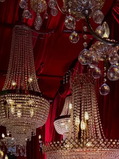 A cluster of ornate crystal chandeliers hanging against a deep red velvet ceiling. This element of our design adds a sense of grandeur and opulence to the entire space.