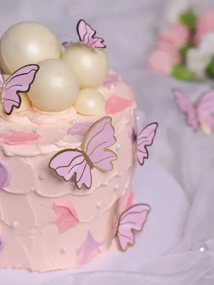 We create a magical garden with this pink butterfly cake. A flurry of pink and gold butterflies appears to dance around the cake, which is decorated with abstract pink frosting and shimmering white chocolate spheres, perfect for a whimsical birthday.