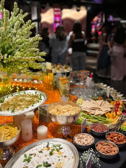 A wide shot of a festive grazing table, beautifully decorated with marigold petals and candles. The spread includes a variety of dips, chips, and nuts, creating an inviting and celebratory atmosphere for guests.