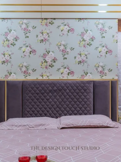A close-up of the bed, showcasing the quilted purple headboard set against the delicate floral wallpaper. The combination of textures and patterns creates a rich and luxurious feel.