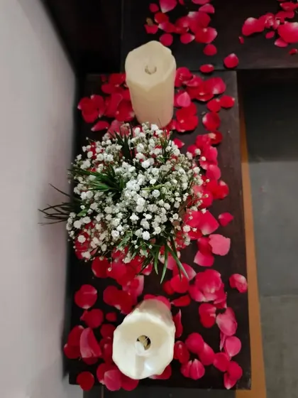 A close-up of decor along an entryway, with candles and a small bouquet of baby's breath scattered among red rose petals.