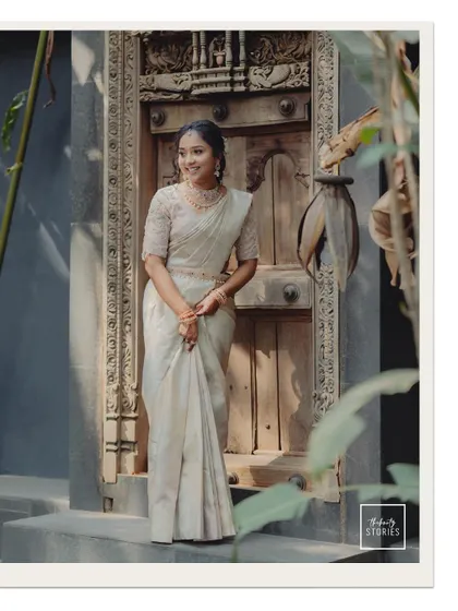 A stunning bridal portrait in a classic white saree, standing by a beautifully carved wooden door.