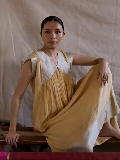 A full-length seated portrait that showcases the relaxed elegance of the garment. The simple setting and direct gaze make the image feel personal and authentic.