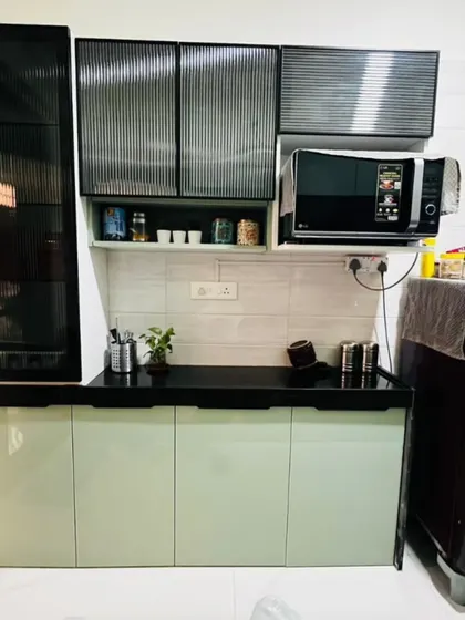 This kitchen combines soft mint-green cabinets with a bold black countertop and fluted glass shutters. The design includes a dedicated space for the microwave, keeping the counter free.
