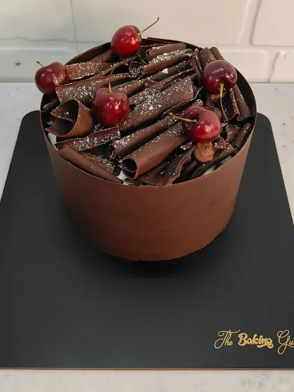 A tall and elegant Black Forest cake, wrapped in a chocolate collar and topped with chocolate curls and fresh cherries. A showstopper for any party.