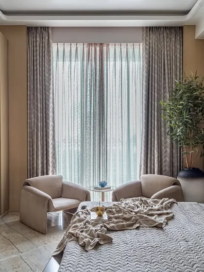 This bedroom exudes warmth and comfort with its soft, neutral palette and wooden wall paneling. A cozy two-chair seating nook by the window provides a perfect spot for morning coffee.