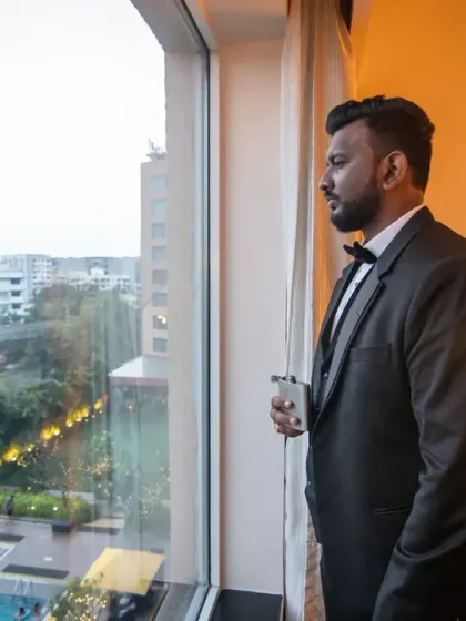 A classic, handsome portrait of the groom looking out the window. The warm indoor light creates a sophisticated and pensive mood.