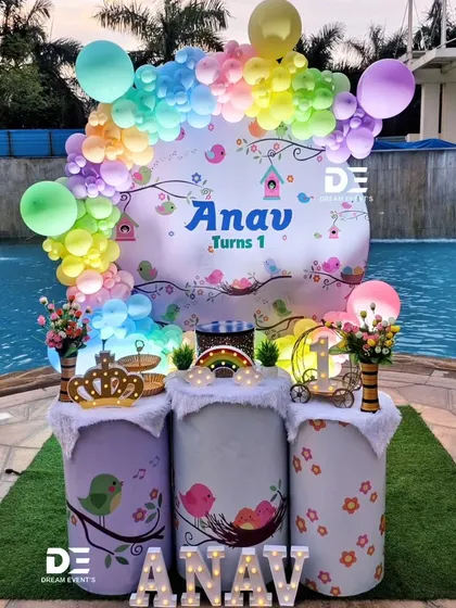 A cheerful bird-themed first birthday for Anav, set against a beautiful poolside backdrop. The setup includes a colorful balloon arch and cute bird illustrations.
