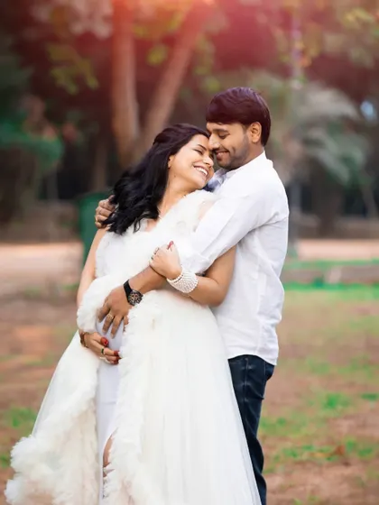 A joyful hug shared by the couple in a park. The expecting mother's smile is radiant, capturing the happiness of this special time in their lives.