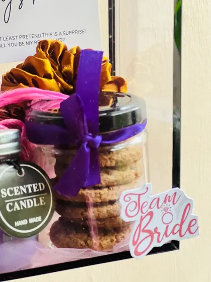 A close-up on the "Team Bride" sticker and the jar of cookies inside a bridesmaid hamper. It highlights the quality of the curated items.