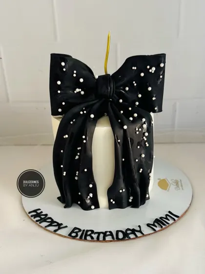 A chic and simple cake featuring a large, dramatic black fondant bow sprinkled with sugar pearls.