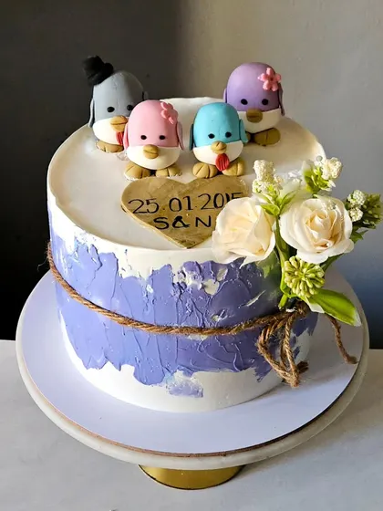 A charming anniversary cake celebrating ten years of family. The cake is topped with a family of four cute, handcrafted penguins, and is finished with a rustic twine wrap and fresh flowers.