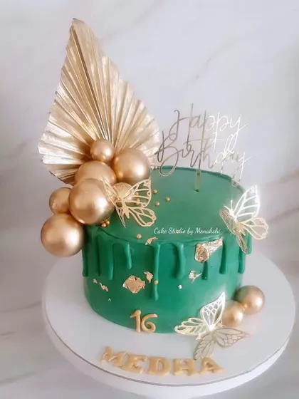 A striking sweet sixteen cake in emerald green and gold. This design features a gold drip, golden butterflies, and a large palm spear for a bold and modern celebration.