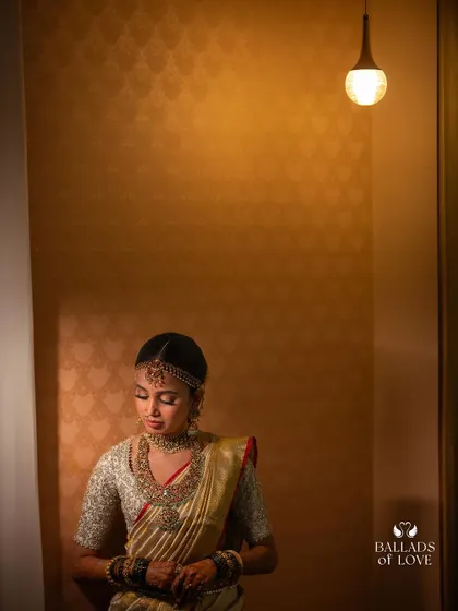 A contemplative portrait of a bride in her gold saree and custom blouse. The lighting highlights the rich texture of the fabric and the detailed embroidery.
