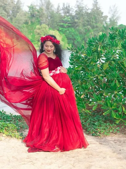 This beautiful red gown with a flowing trail is perfect for a maternity shoot by the water, creating a stunning and dramatic look.