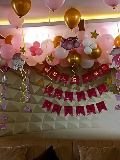 A "Welcome Home" setup for a baby girl, with pink and gold balloons and themed banners over a sofa.