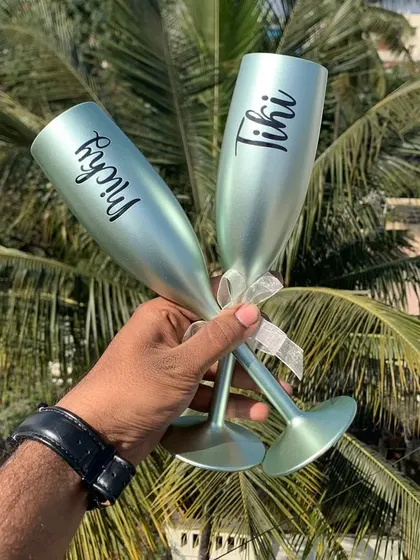 A pair of light green unbreakable champagne flutes, customized with names. They are perfect for outdoor celebrations or as a unique couple's gift.