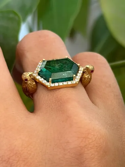 A one of a kind swivel ring. This playful piece features a differently cut emerald and diamonds set in 18k gold, with two tiny birds holding the central stone.