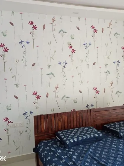 A delicate floral wallpaper installed as an accent wall in a bedroom. The pattern adds a soft, calming feel to the sleeping space.
