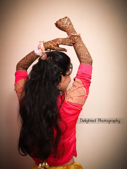 An artistic shot of the bride showing off her elaborate mehndi design, with her arms raised in a graceful pose.