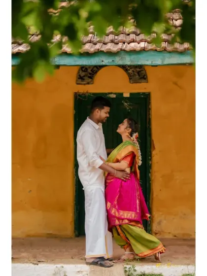 A sweet pre-wedding portrait in a rustic village setting. The vibrant colors of their outfits stand out against the traditional backdrop.