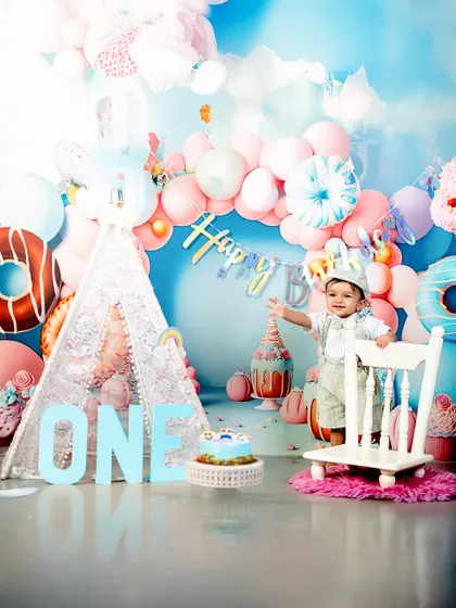 Every first birthday deserves a grand celebration. This little boy looks absolutely regal in his party hat, standing by his cake in a beautifully decorated studio setting.