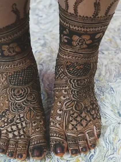 This intricate foot mehendi features a combination of floral patterns and traditional motifs. The design provides heavy coverage on the top of the foot while leaving some skin exposed for a beautiful contrast.