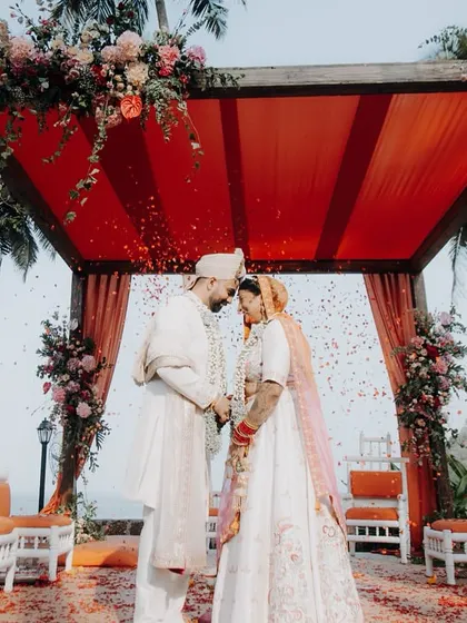 A beautiful moment under the mandap at a Goa wedding, with the couple sharing a quiet forehead touch as flower petals rain down.