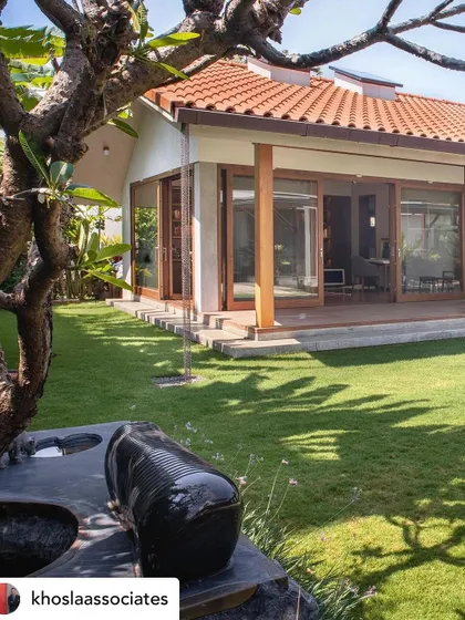 A view across a manicured lawn towards a modern villa, with a custom stone music bench in the foreground. The landscape is designed with clean lines and open spaces, creating a sensory experience that connects with the home's architecture.