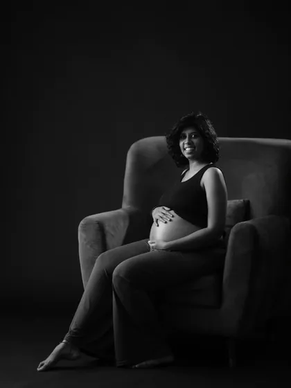 A striking black and white portrait in a comfortable armchair. The dark background and focused lighting create a moody and sophisticated look.
