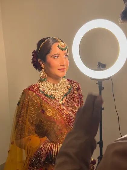 Behind the scenes with a ring light, capturing the beautiful details of this multi-colored floral bun and the bride's radiant look.