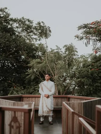 A portrait of the groom in his wedding attire, standing on a wooden deck surrounded by nature, looking calm and ready.