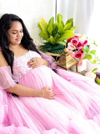A peaceful portrait of a mom-to-be relaxing in a beautiful pink gown, surrounded by flowers and greenery.