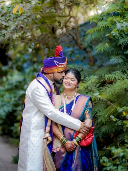 A romantic portrait of the groom embracing his bride from behind and kissing her forehead.