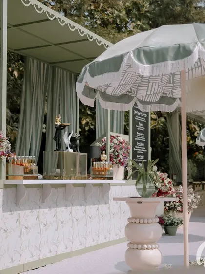 The bar area, complete with stylish umbrellas and custom-designed high tables. The front of the bar features a delicate floral pattern, tying it into the overall garden aesthetic.