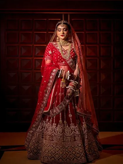 A full-length bridal portrait using dramatic lighting to create a powerful and elegant image of the bride in her red lehenga.