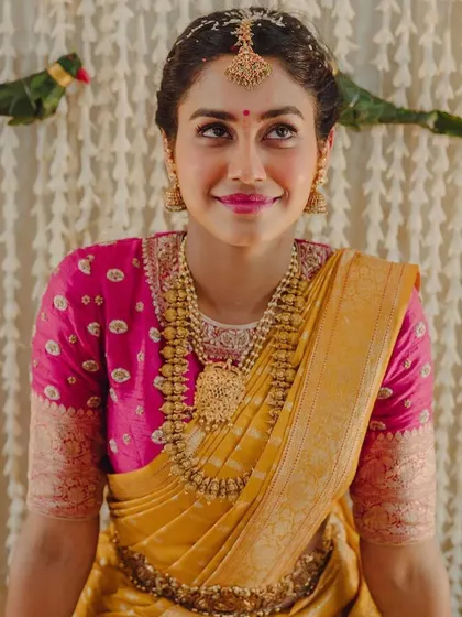 A bride in a yellow and pink Kanchipuram saree. Her custom pink blouse features delicate butti embroidery, perfect for a pre-wedding pooja.