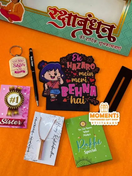 We haven't forgotten the sisters! This Rakhi return gift combo for sisters includes a tabletop, pen, mirror card, magnet, keychain, and a bar pendant necklace.