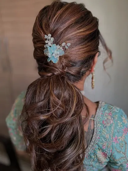 A voluminous ponytail with soft curls and a pretty blue floral accessory. This hairstyle is perfect for a reception or cocktail party.